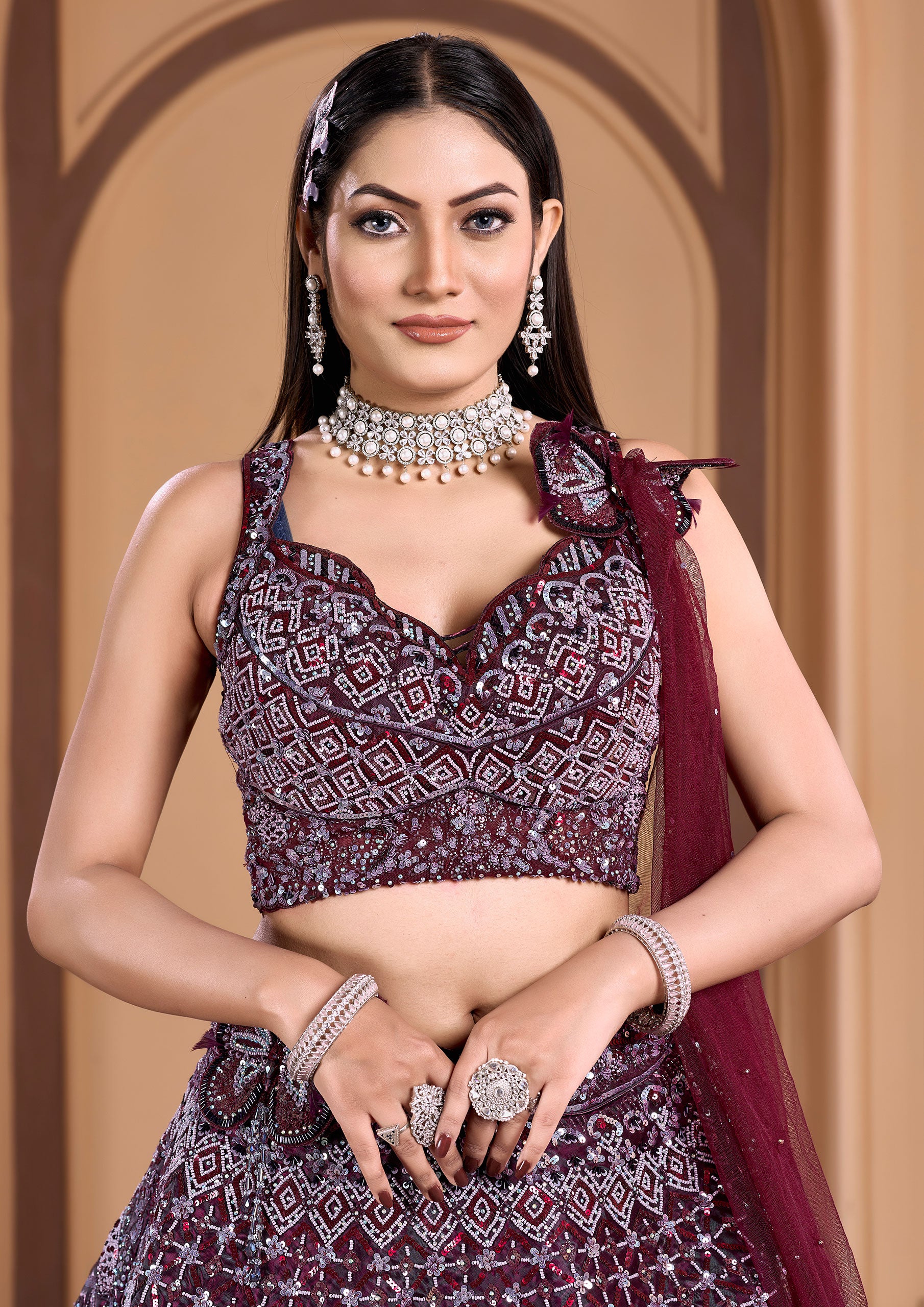 A stunning woman in a wine lehenga and matching blouse, adorned with elegant jewelry.